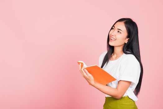 Portrait of happy Asian beautiful young woman confident smiling standing holding orange book open or diary for reading, studio shot isolated on pink background, with copy space, education concept