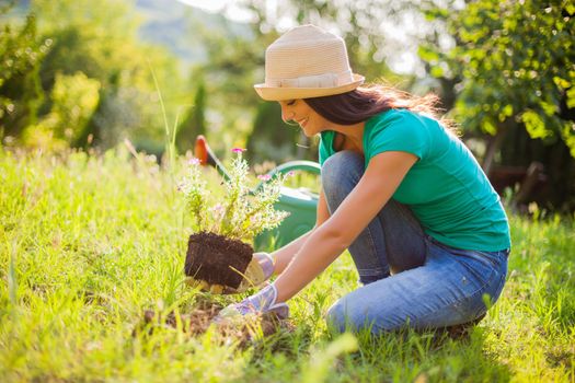 Young happy woman is planting a flower in her garden.