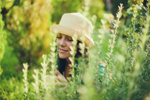 Young happy woman is enjoying the smell of rosemary in her garden.