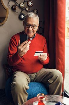 Senior man is sitting in cafe and shopping online.