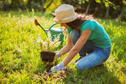 Young happy woman is planting a flower in her garden.