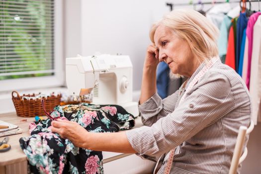 Adult woman is sewing in her studio. She is frustrated because she made a mistake.