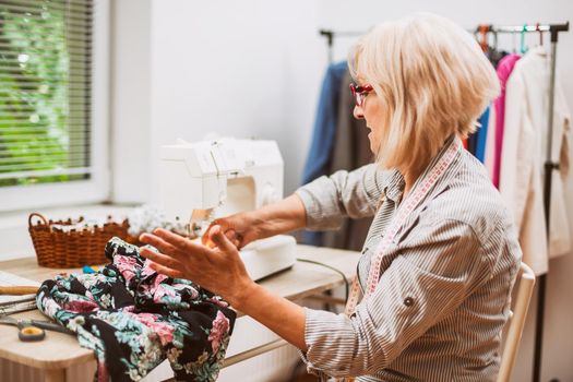 Adult woman is sewing in her studio. She is frustrated because she made a mistake.