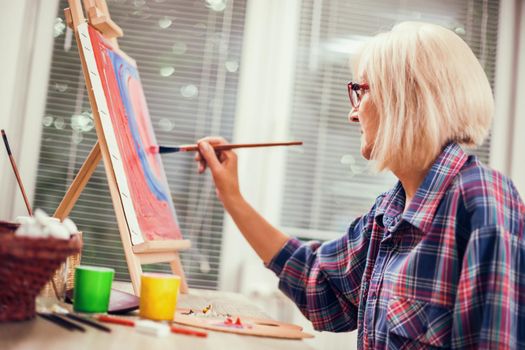 Elderly woman is painting in her home. Retirement hobby.