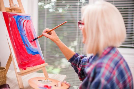 Elderly woman is painting in her home. Retirement hobby.