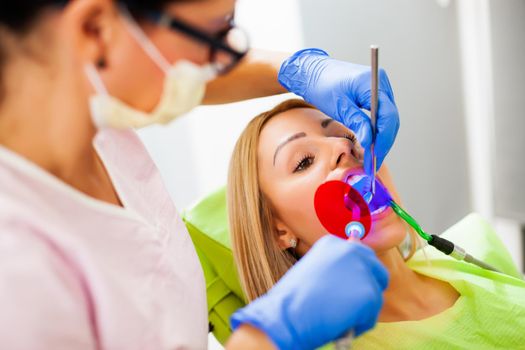 Young woman at dentist. Dentist is repairing her teeth.