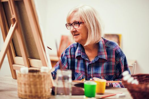 Elderly woman is painting in her home. Retirement hobby.