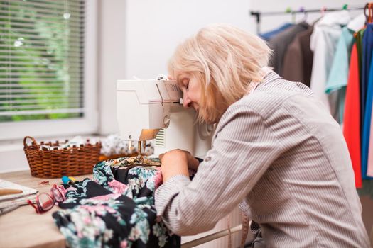 Adult woman is sewing in her studio. She is tired.