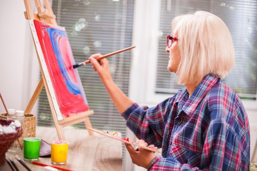 Elderly woman is painting in her home. Retirement hobby.