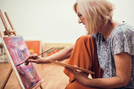 Elderly woman is painting in her home. Retirement hobby.