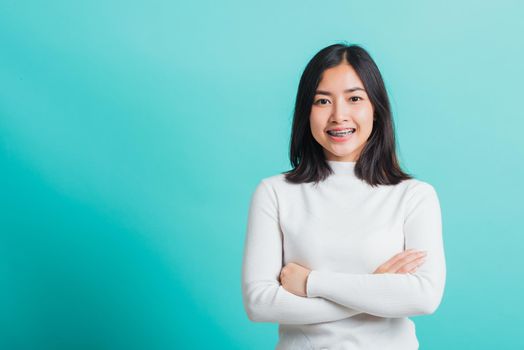 Young beautiful Asian woman smiling with crossed arms, Portrait of positive confident female stand cross one's arm, studio shot isolated on a blue background