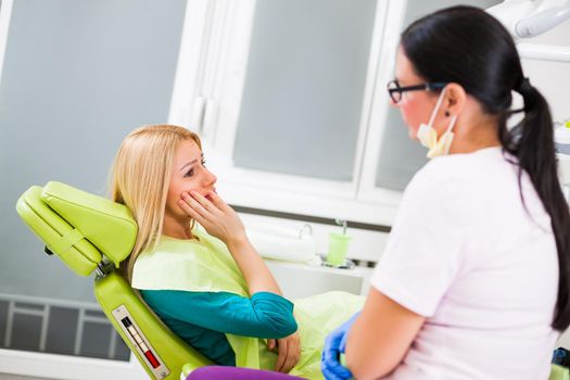 Young woman at dentist. She has toothache.