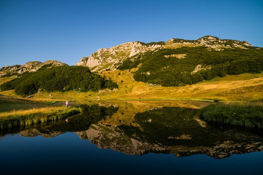 Photographer taking photo on mountain lake in summer.