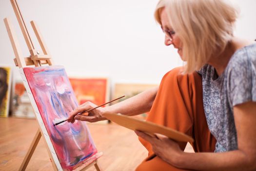 Elderly woman is painting in her home. Retirement hobby.