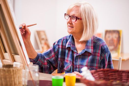 Elderly woman is painting in her home. Retirement hobby.