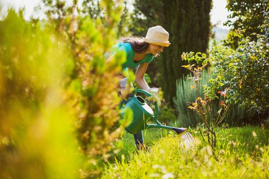 Young woman in her garden. She is watering plants.