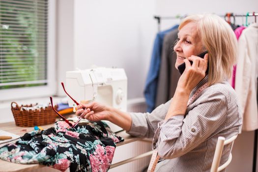 Adult woman is sewing in her studio. She is talking with client.