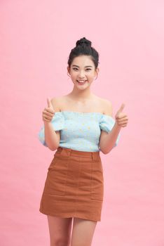 Pretty asian woman standing over pink background smiling and doing the ok signal with her thumbs
