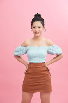  Smiling young woman standing with arms akimbo on waist isolated on pink pastel wall 