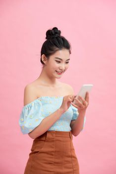 Excited Asian girl using smartphone standing over pink background. Empty Space