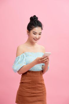 Excited Asian girl using smartphone standing over pink background. Empty Space