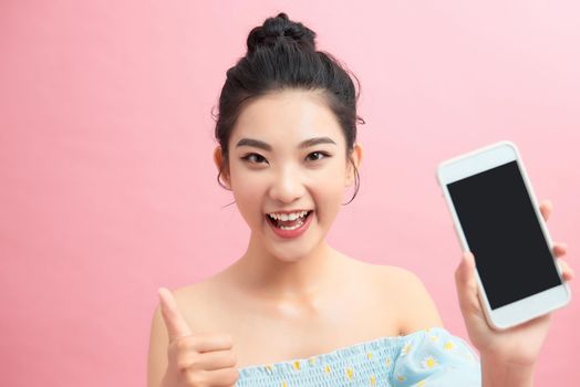 Pretty woman smiling holding holding using smartphone posing on pink background isolated smiling having fun, showing phone screen
