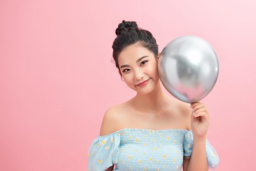 A woman holding silver balloon against a pink background
