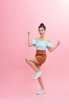 Portrait of an excited asian woman jumping and looking at camera isolated over pink background