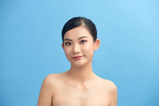 Beautiful face of young adult woman with clean fresh skin and bare shoulders on blue background.