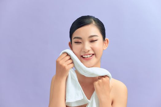 Beautiful happy smiling young asian female model wiping facial skin with soft towel, removing makeup