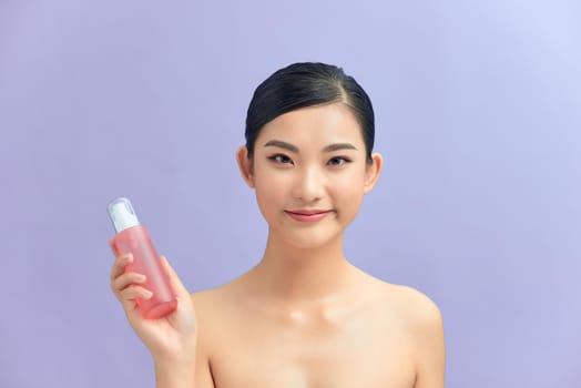 Portrait of a beautiful young girl standing isolated over color background, showing body lotion bottle