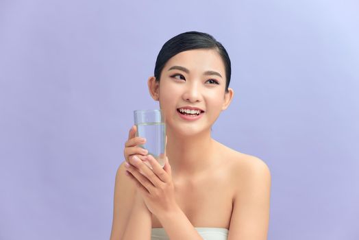 Smiling beautiful young lady holding a glass of drinking water. Isolated in color background.