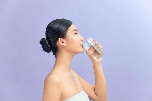 Attractive woman drinking water against purple background
