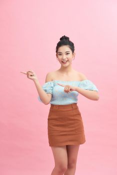 Beautiful asian woman pointing to copy space. isolated on pink background.