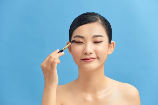 Closeup shot of beautiful woman applying eyeshadow on eyelid using makeup brush
