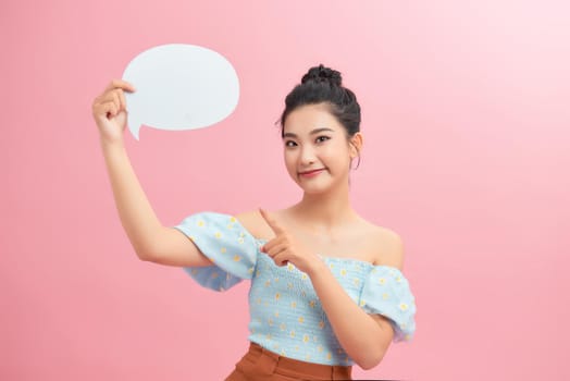 Portrait of an excited young woman holding empty speech bubble and pointing finger up isolated over pink background
