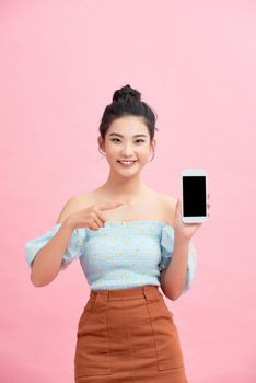 Portrait of an excited young woman showing blank screen mobile phone isolated over pink background