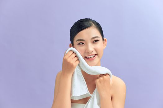 Beautiful happy smiling young asian female model wiping facial skin with soft towel, removing makeup