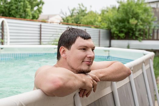 Young smiling man leaning on the side of the swimming pool, swimming in the pool