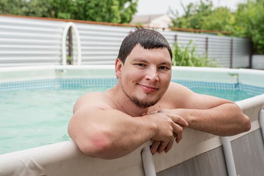 Young smiling man leaning on the side of the swimming pool, swimming in the pool