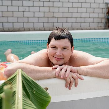 Young smiling man leaning on the side of the swimming pool, swimming in the pool