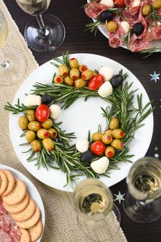 An appetizer of rosemary stuffed with olives with baby mozzarella and cherry tomatoes. Made in the form of a Christmas wreath.