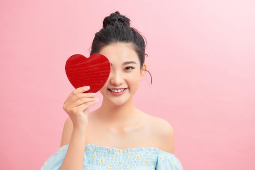 Waist-up portrait of pretty Asian woman looking away with toothy smile while holding Valentines Day card in hands