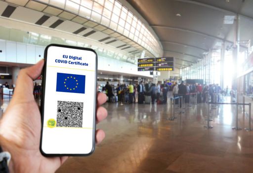 EU Digital COVID Certificate with the QR code on the screen of a mobile held by a hand with blurred airport in the background. Immunity from Covid-19. Travel without restrictions.