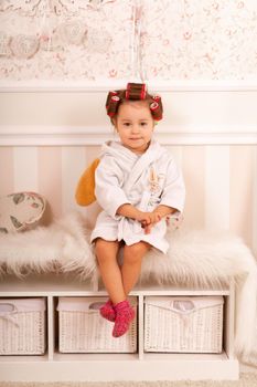 Adorable little girl with curlers paints her fingernails. Copies mom's behavior. Young fashionista. Beauty day.