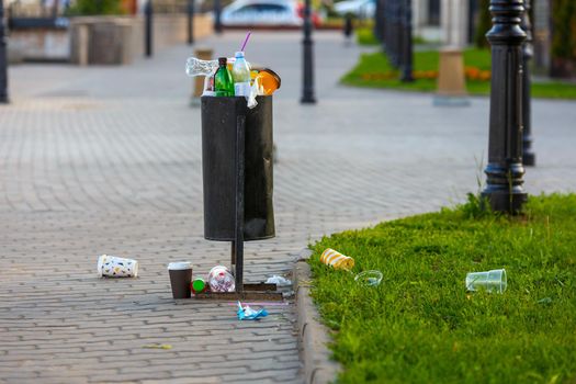 overflowing trash can on the sidewalk pavement at summer daylight.