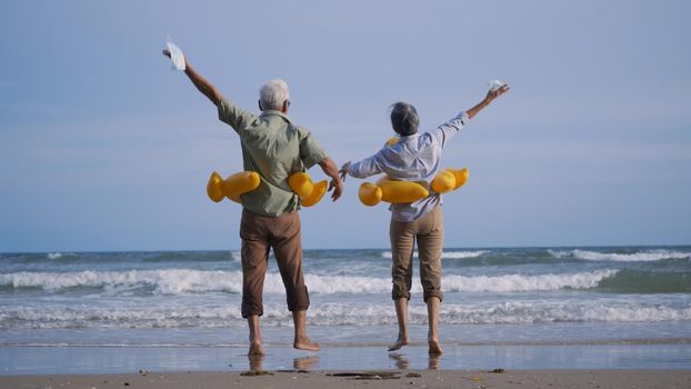 Happy senior couple wear rubber ring take off medical face mask and running to the beach enjoying life, relaxing after win coronavirus pandemic (COVID-19), plan life insurance at retirement couple