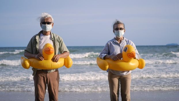 Happy senior couple wear rubber ring take off medical face mask and running to the beach enjoying life, relaxing after win coronavirus pandemic (COVID-19), plan life insurance at retirement couple