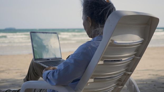 Senior woman relax sitting on chairs enjoying time on beach travel vacation working with laptop computer, Romantic elderly enjoy Travel summer vacation, plan life insurance at retirement concept