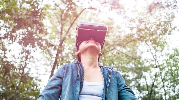 Happy woman wearing VR-headset glasses of virtual reality in forest and enjoying the nature on a sunny summer day in spring garden. Modern technology concept.